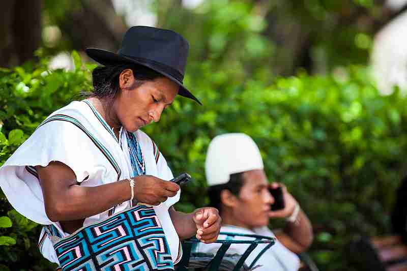 Two Arhuaco men in traditional clothes using phones